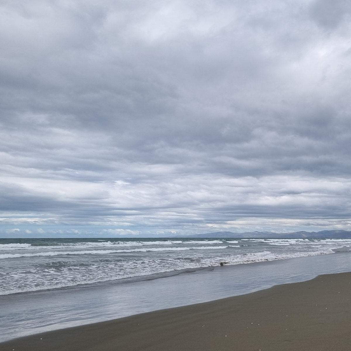 Pegasus Bay, Canterbury — grey skies, rolling waves and the Canterbury Port Hills on the horizon, New Zealand.